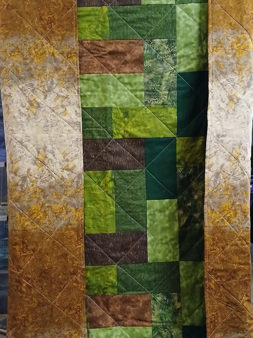 Vertical quilt with green, brown, and gold patchwork panels and cream patterned borders
