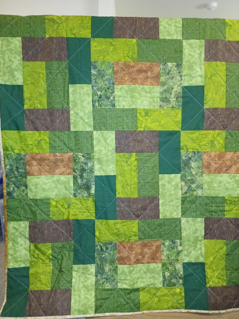 Green and brown patchwork quilt with geometric rectangles and squares, viewed flat against a background.