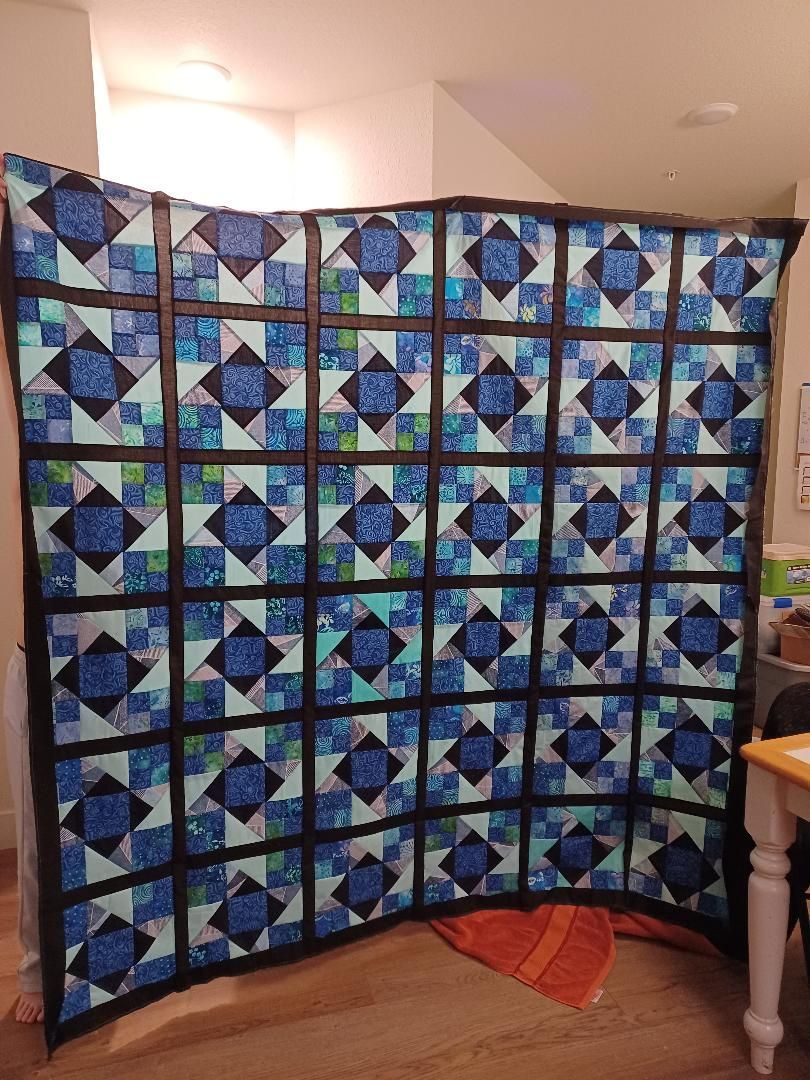 Blue and teal quilt with geometric blocks hanging across a room corner