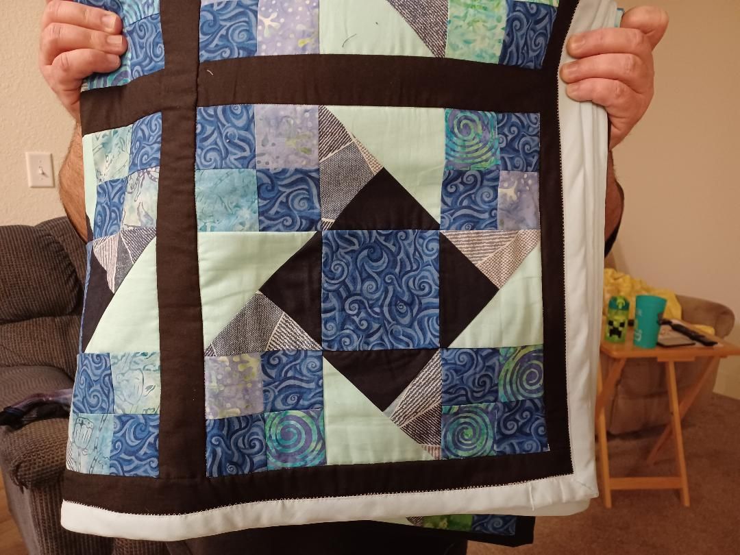 Person holding a blue, white, and black quilt with geometric patchwork pattern