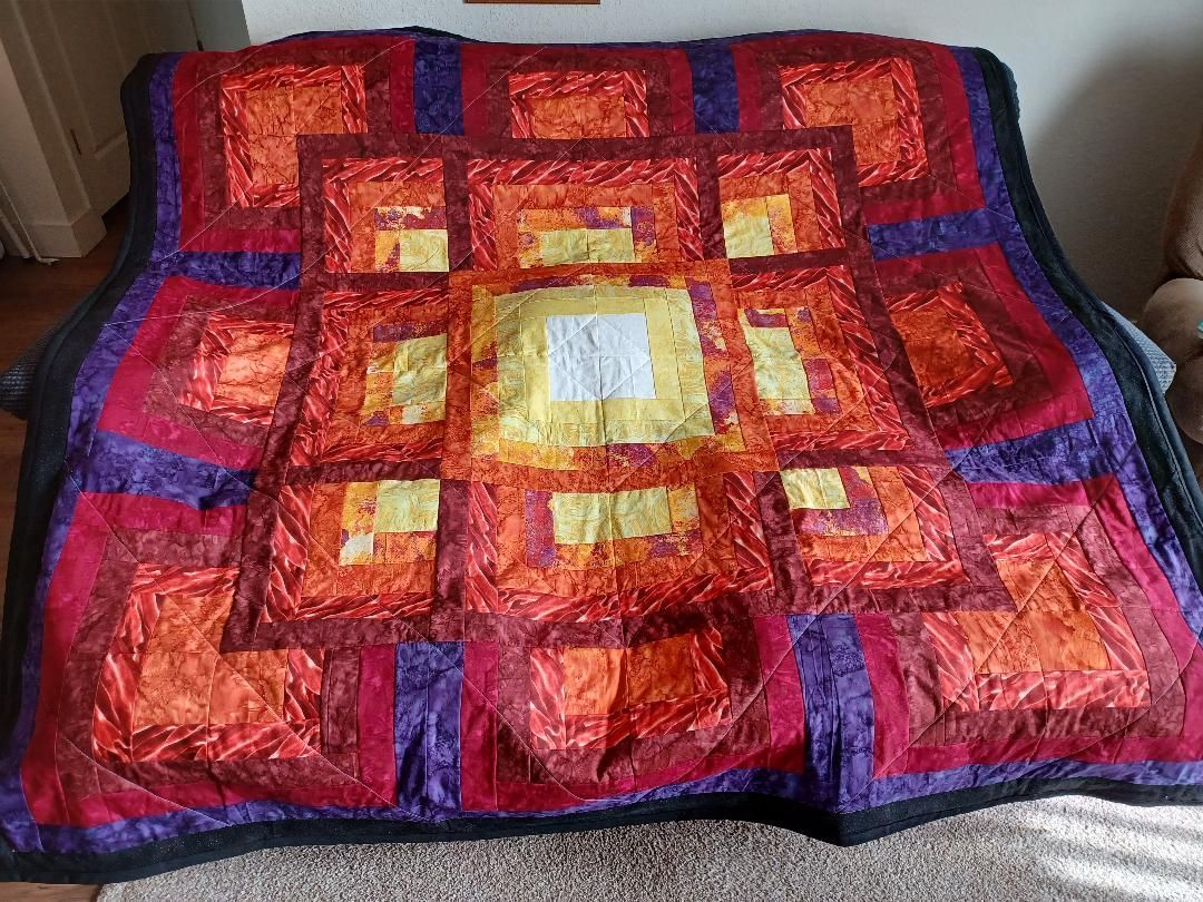 Colorful red, orange, and yellow patchwork quilt with a dark blue border draped over a couch.