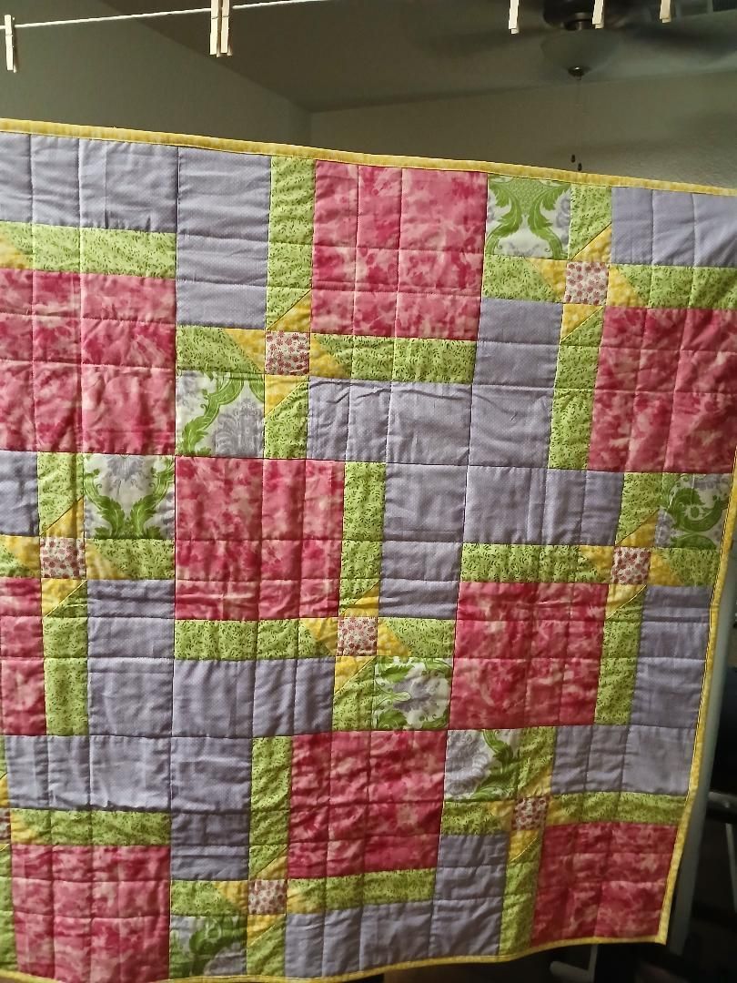 Pink, green, and lavender patchwork quilt hanging indoors on a clothesline.