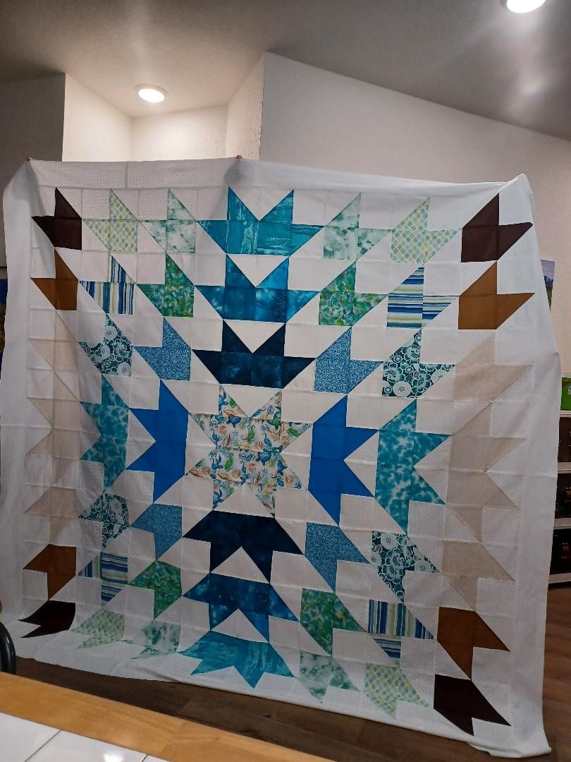 Blue and teal star quilt hanging indoors on a wall, with brown corner blocks