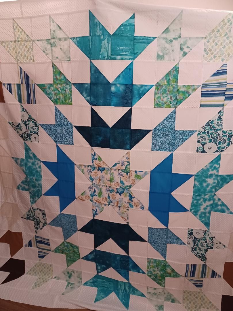 Blue and teal starburst patchwork quilt with floral fabric accents on a white background