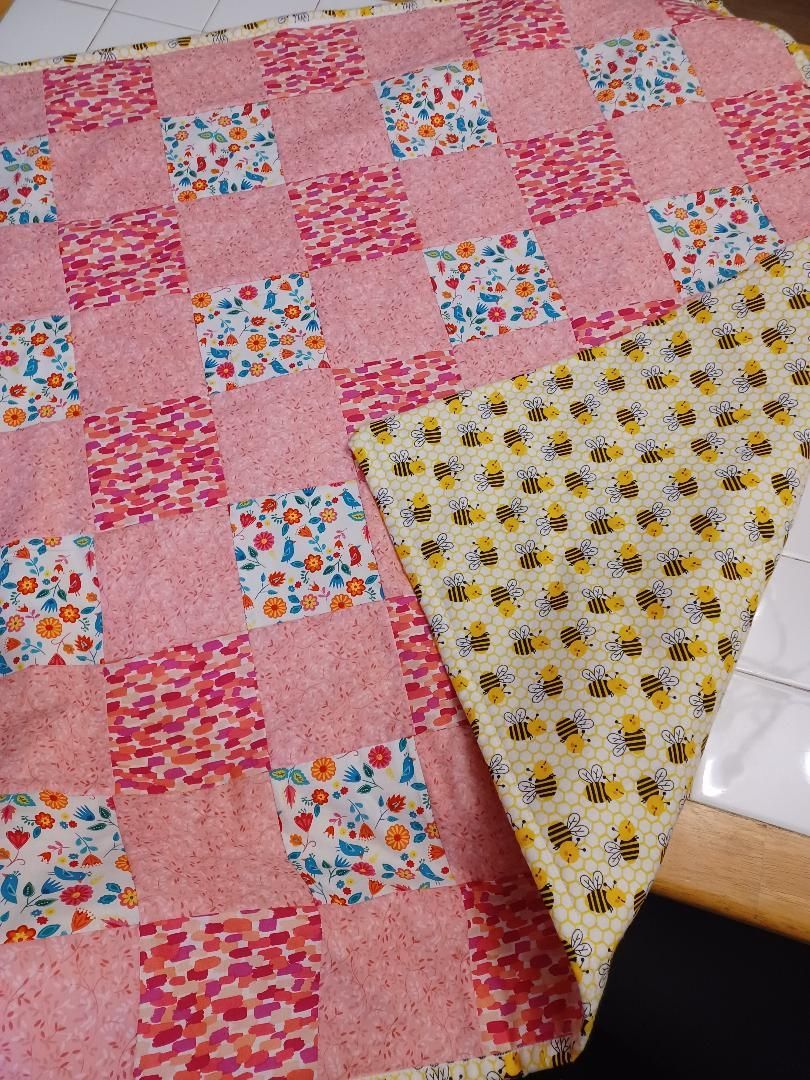 Pink patchwork quilt with floral squares and a yellow bee-print backing folded over a corner