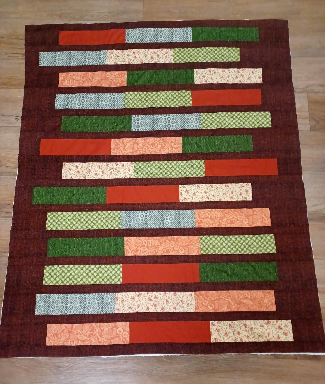 Rectangular patchwork quilt with horizontal stripes in red, green, beige, and brown tones