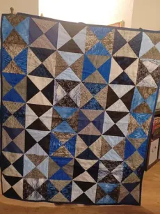 Patchwork quilt of blue, gray, brown, and white geometric triangles hanging on a wall