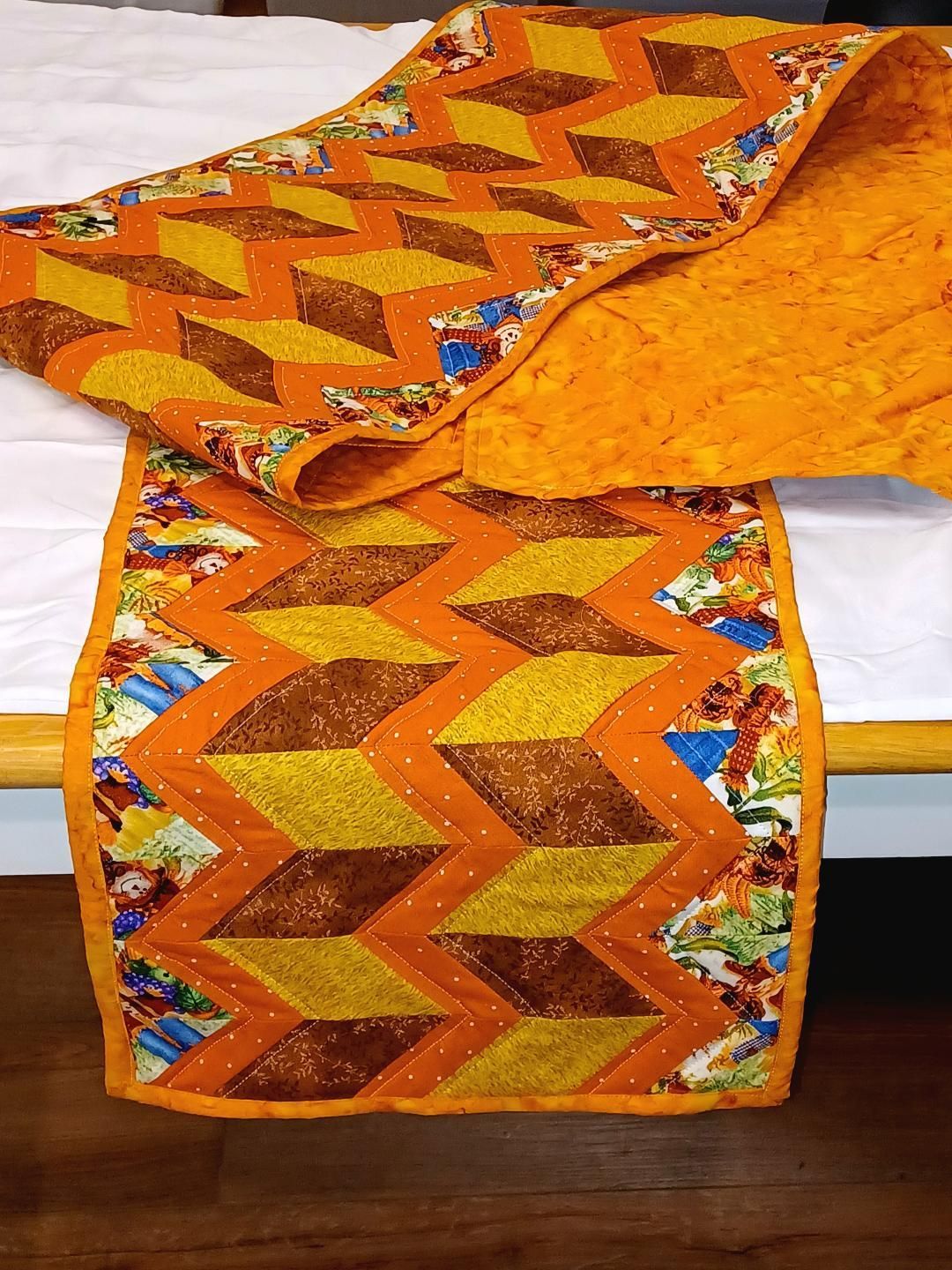 Colorful orange and yellow patchwork quilt with zigzag patterns draped over a bed.