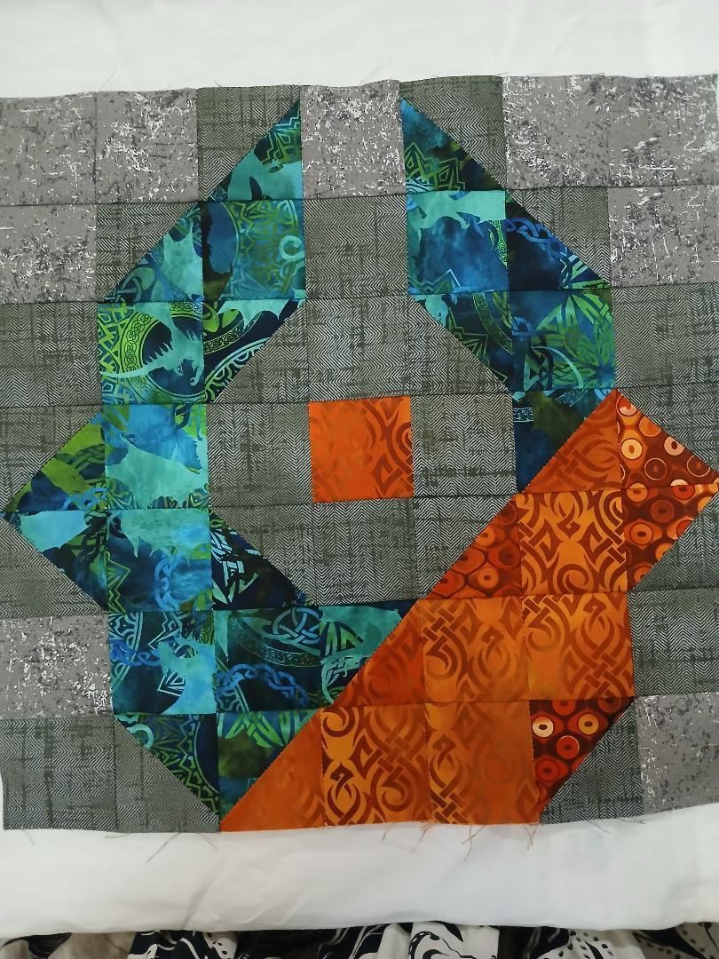 Abstract quilt with teal and blue arcs around a gray center, orange square, and orange diagonal strip on a gray background