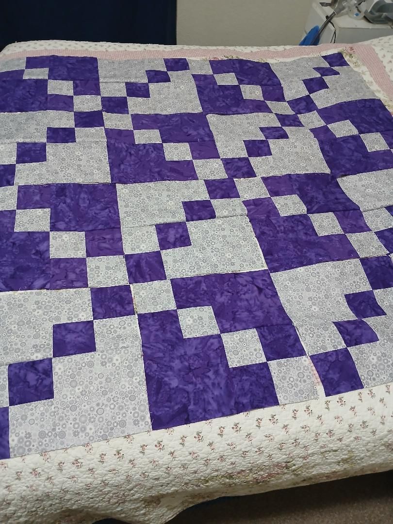 Purple and white patchwork quilt with geometric zigzag pattern on a bed