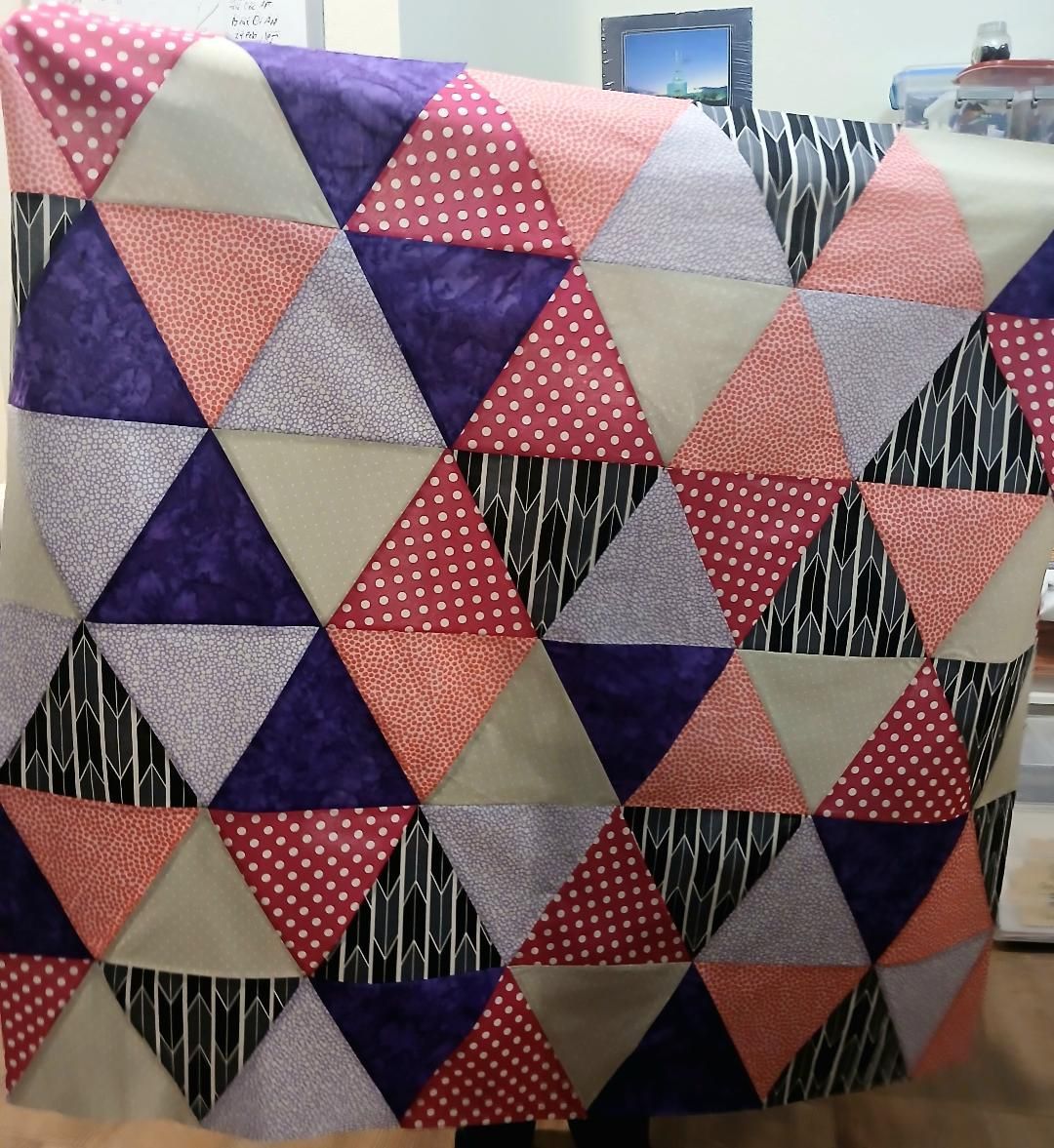 Colorful quilt with triangle patchwork in purple, pink, gray, black, and white patterns.