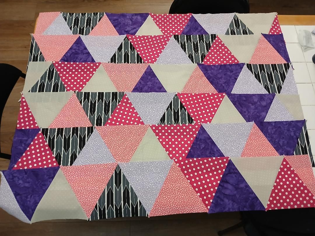 Colorful patchwork quilt with pink, purple, gray, black, and cream triangles arranged in rows
