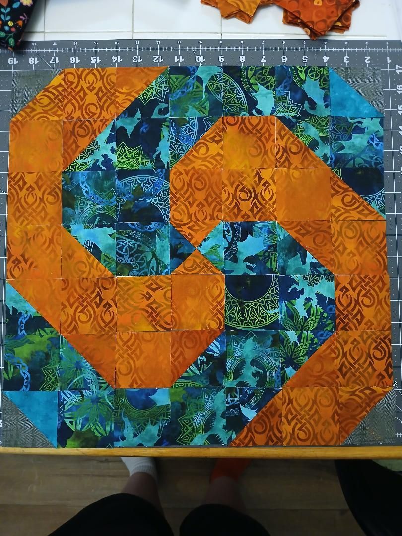Orange and blue geometric quilt blocks forming a swirling pattern on a table