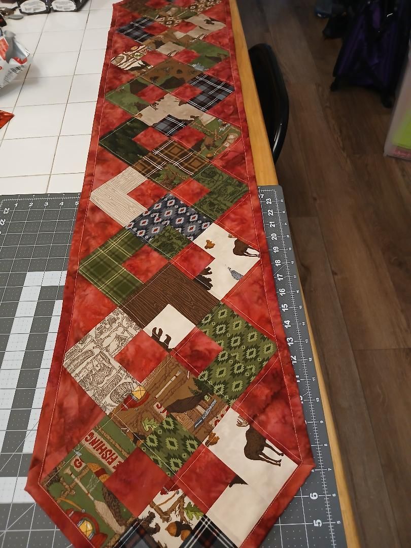 Red and green patchwork quilt runner laid out on a table, with diamond and square patterns.