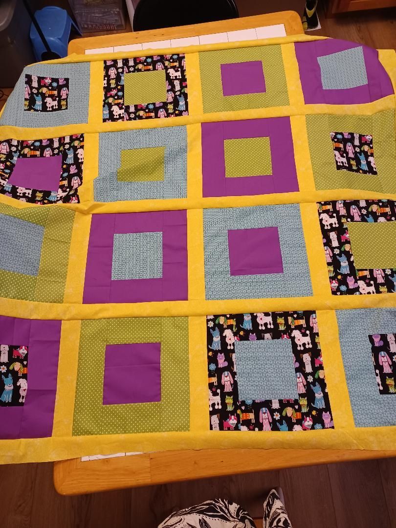 Colorful patchwork quilt with purple, yellow, orange, and patterned square blocks on a bed
