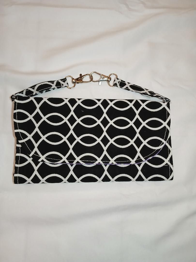 Black-and-white patterned clutch purse with gold chain strap on white fabric background