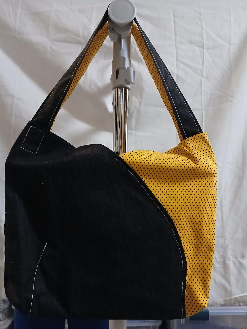 Black and yellow tote bag hanging on a silver hook against a light fabric background