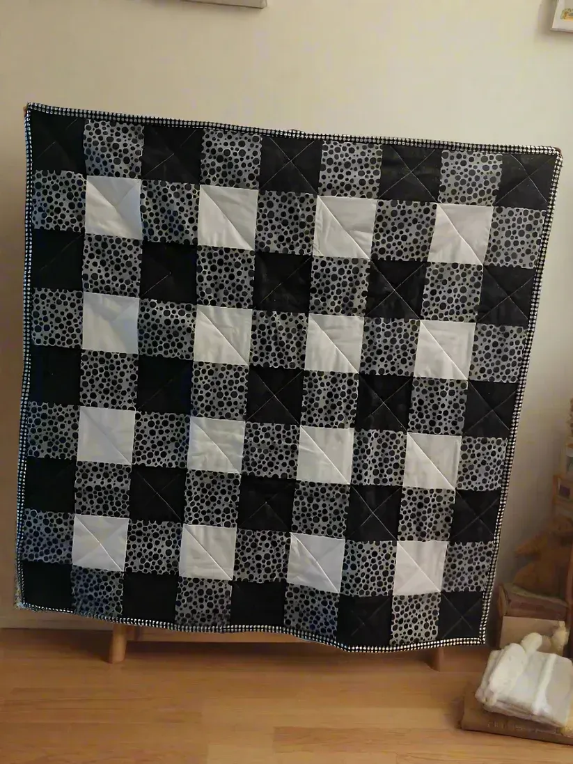 Black-and-white checkered quilt draped over a chair in a room with a wooden floor.