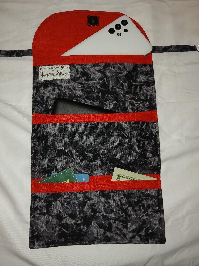 Red-and-black handmade fabric pouch with three horizontal red bands and small decorative pieces.