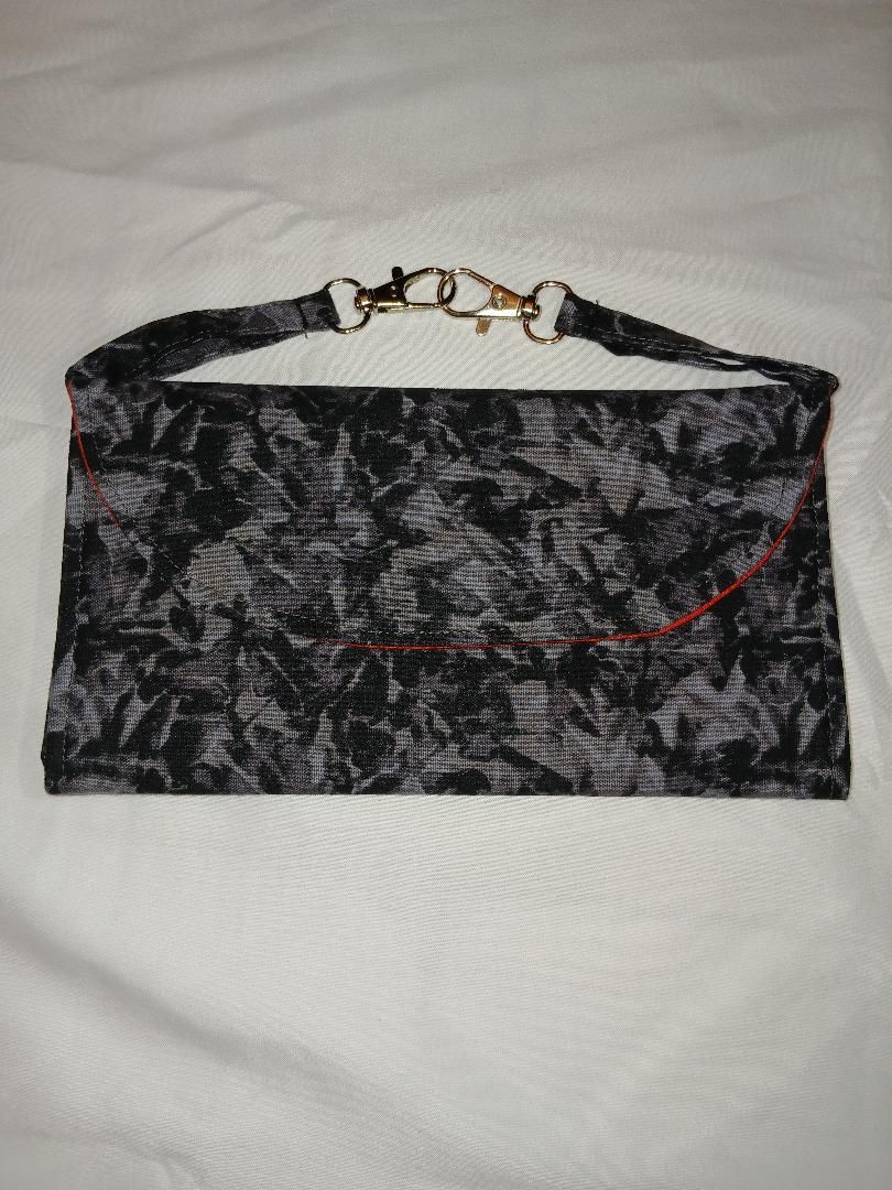 Black marbled handbag with red piping and gold chain handle on a white quilted surface