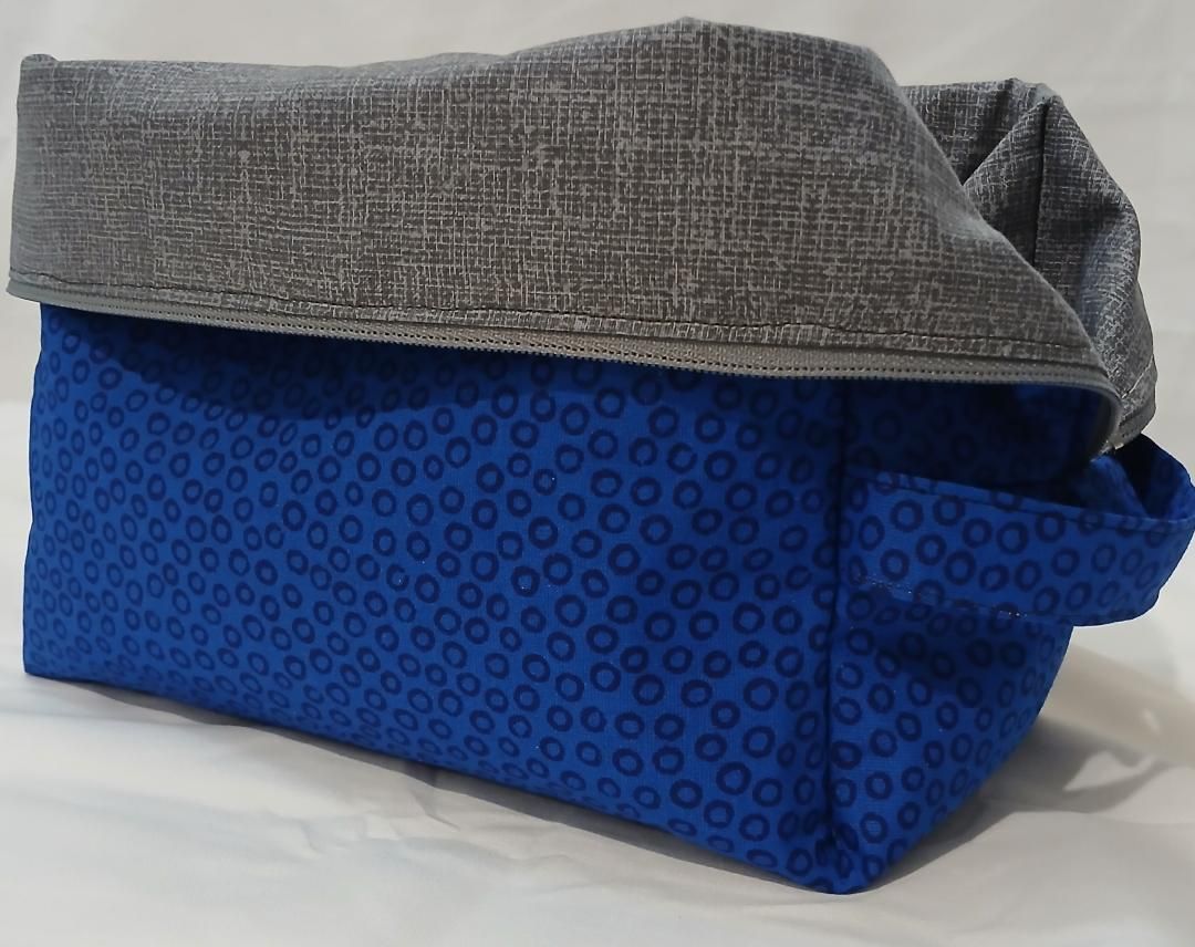 Blue patterned bag with a gray folded flap on top, resting on a white surface