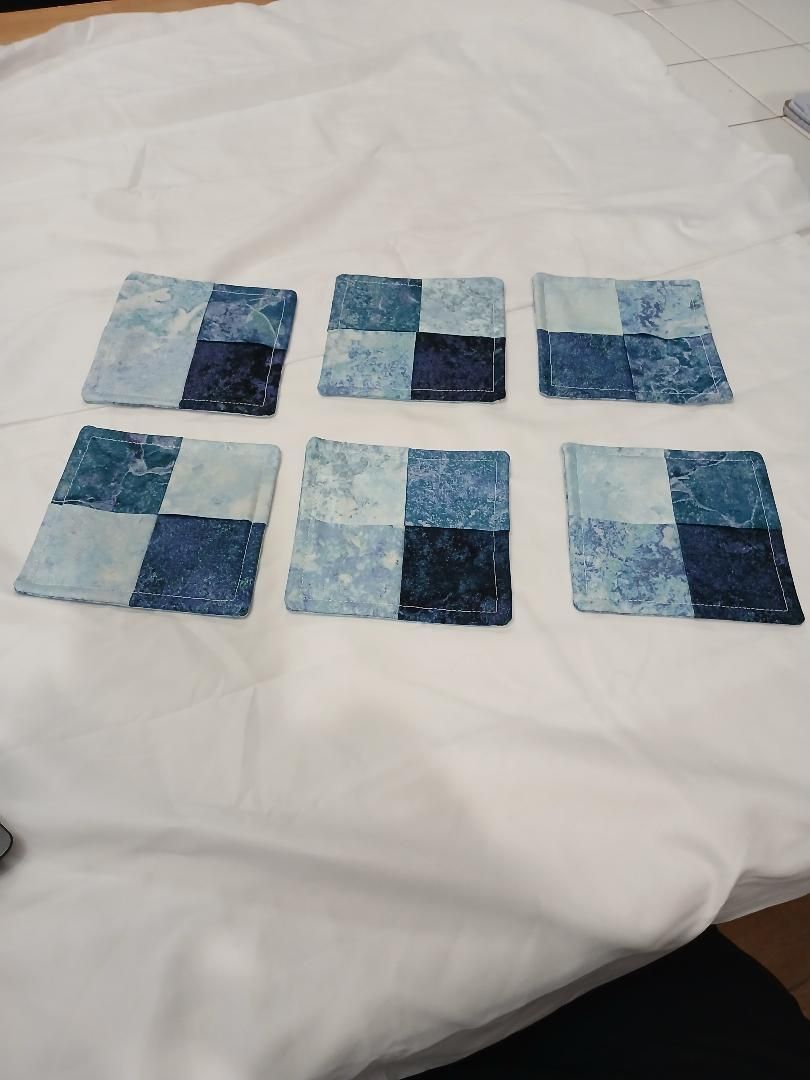 Six blue patchwork fabric squares laid out on a white bedspread.