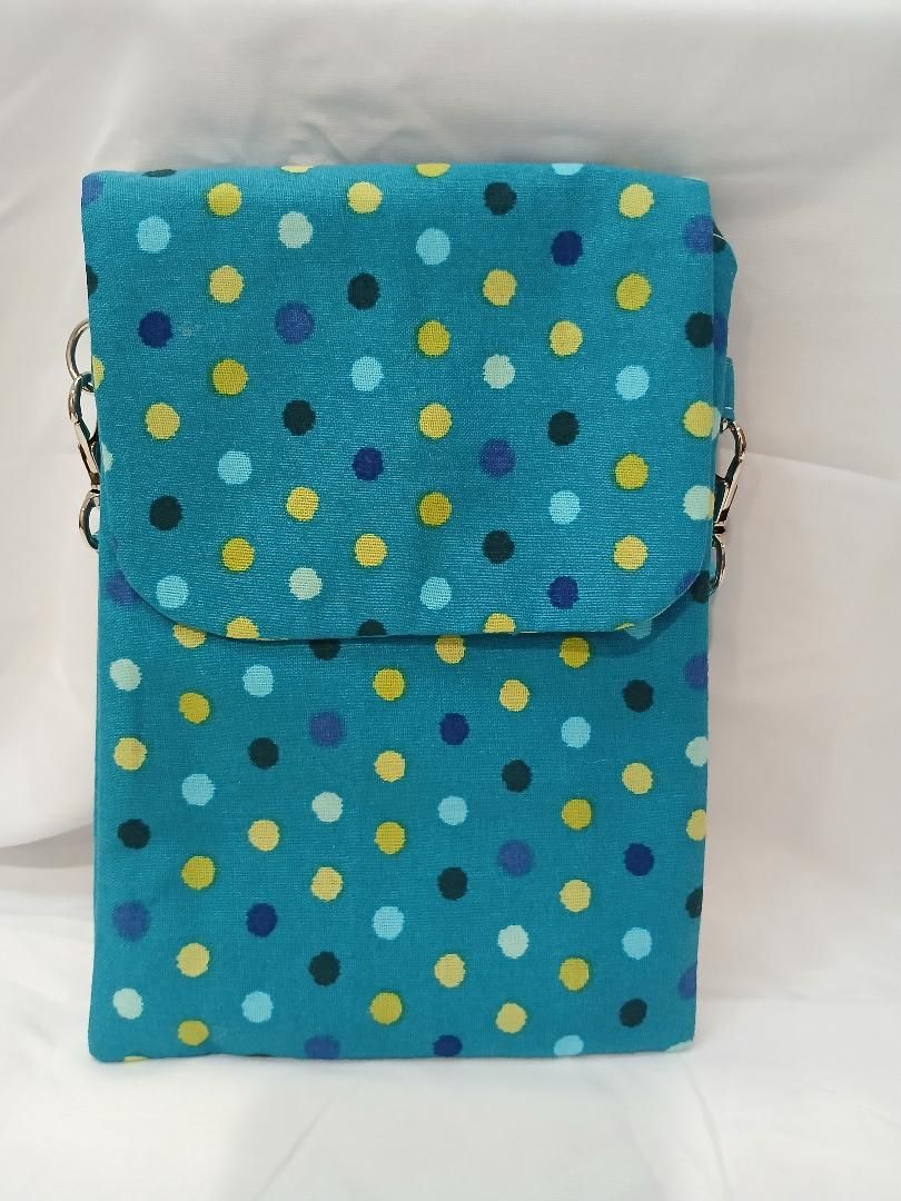 Blue polka-dot fabric pouch with flap and shoulder strap on a white background