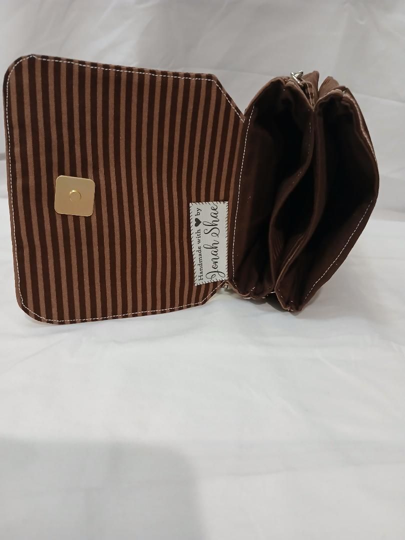 Brown striped fabric bag with a flap and open top, showing a white label and gold button clasp.