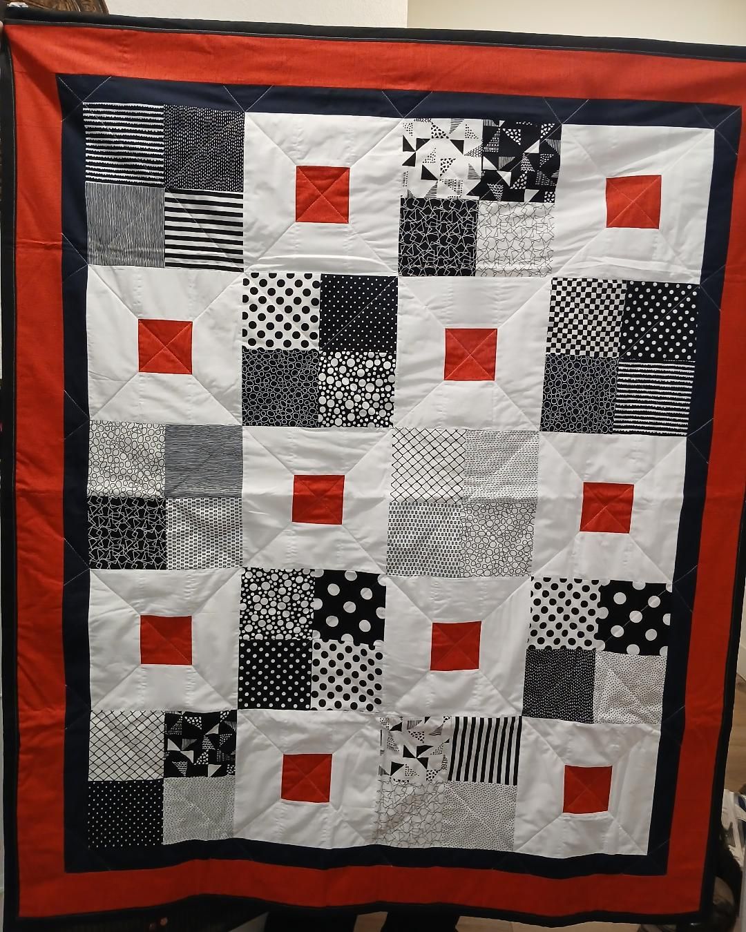 Black, white, and red patchwork quilt with a red border hanging on a wall.