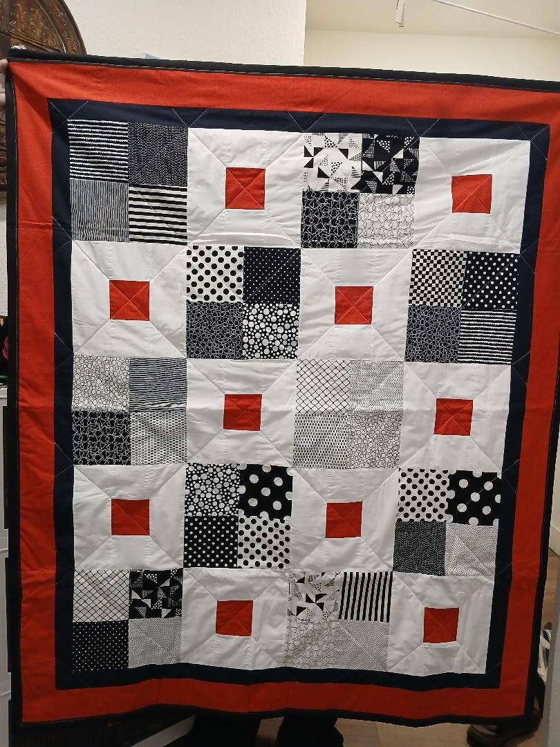 Patchwork quilt with black, white, gray, and orange-red squares and border hanging on a wall