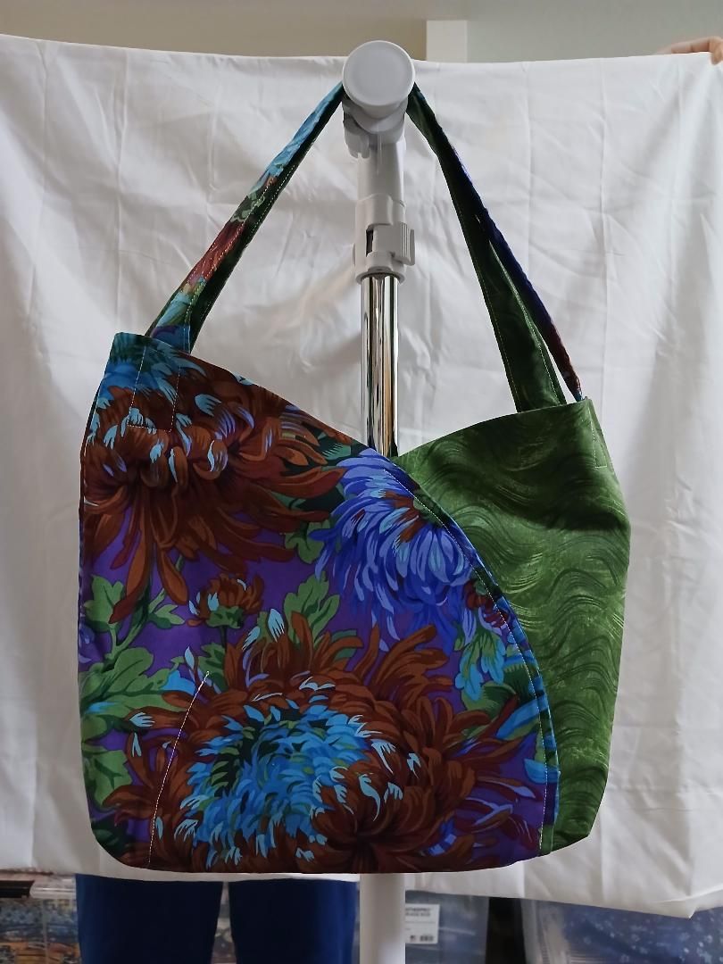Colorful floral tote bag with blue, purple, and green panels hanging on a white display stand