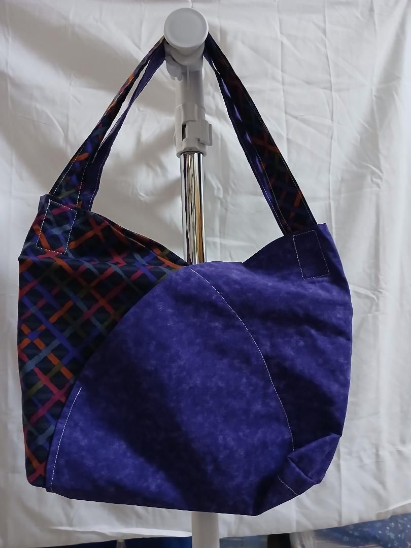Purple and plaid shoulder bag hanging on a white stand against a white backdrop