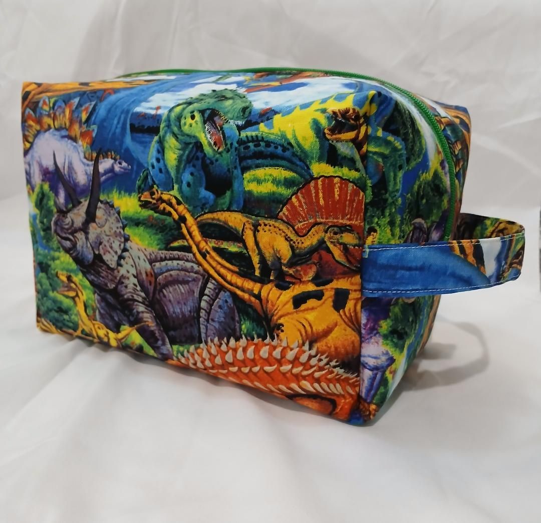 Colorful dinosaur-print fabric pouch with a blue handle on a white background