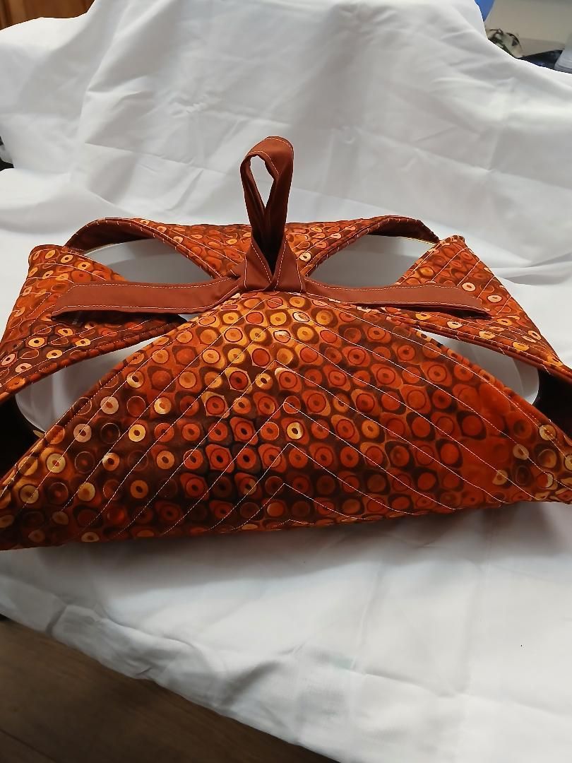 Orange patterned fabric purse with a curved handle on a white cloth background