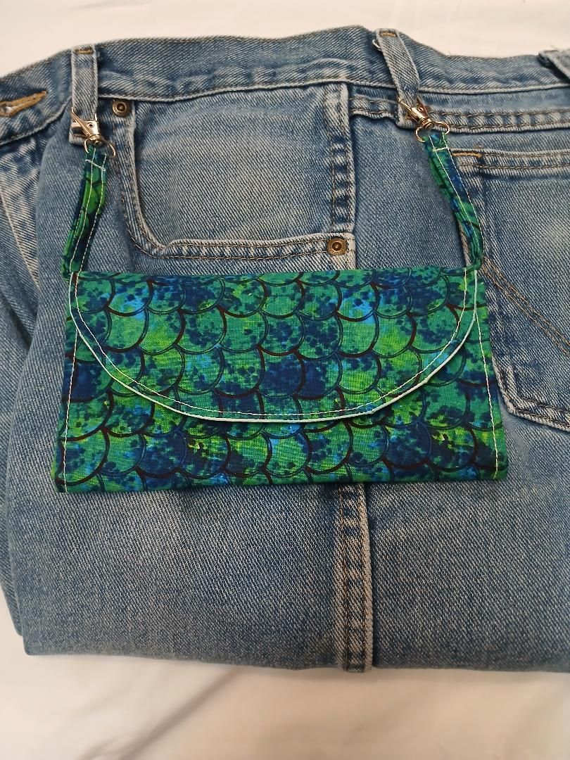 Blue-green patterned purse hanging on the back of faded denim jeans