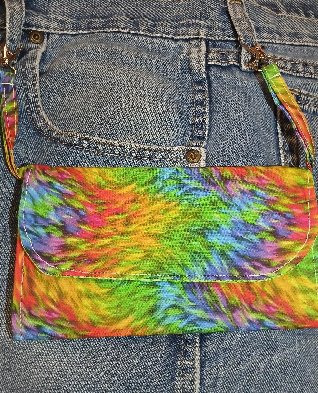 Tie-dye rainbow crossbody bag on blue denim jeans.