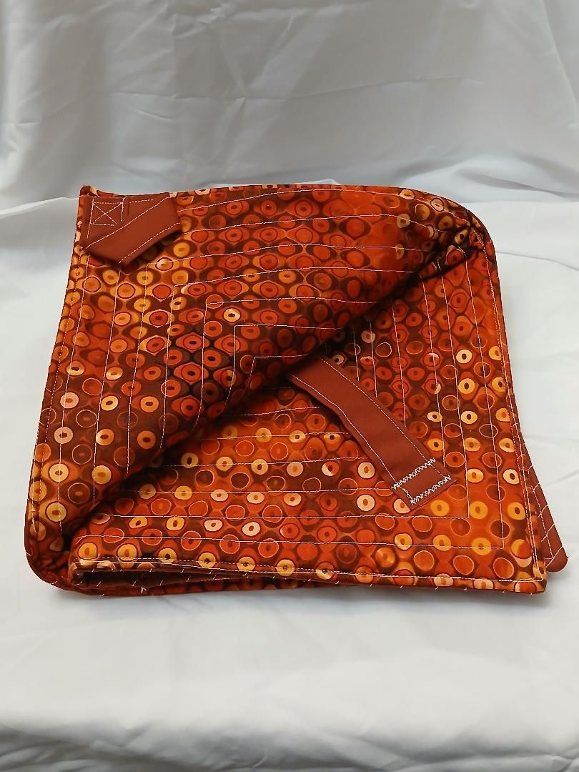 Orange patterned folded cloth with a triangular flap on a white surface