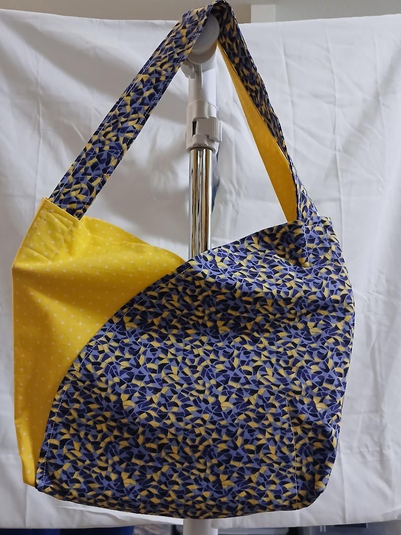 Blue, yellow, and floral patterned shoulder bag hanging from a stand against a white backdrop