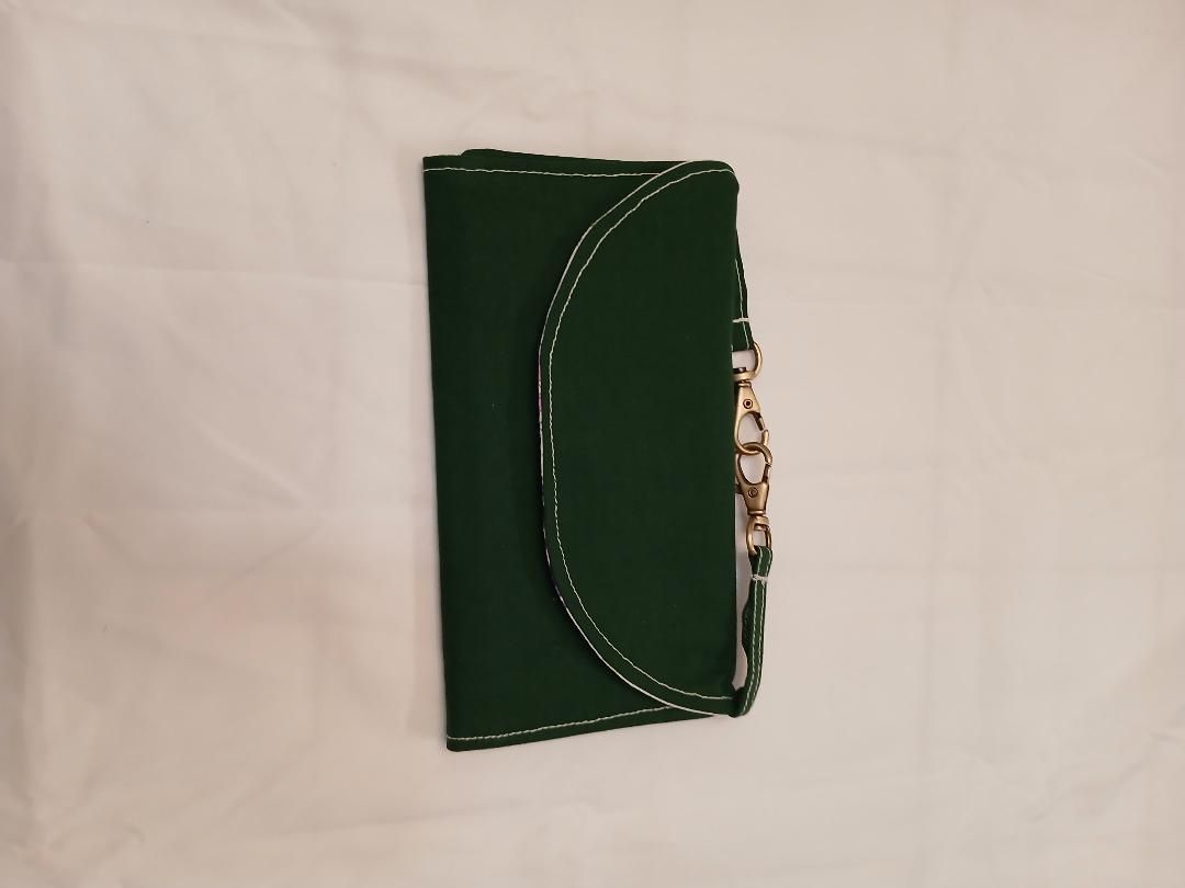Green handbag with a curved flap and gold chain detail on a light fabric background