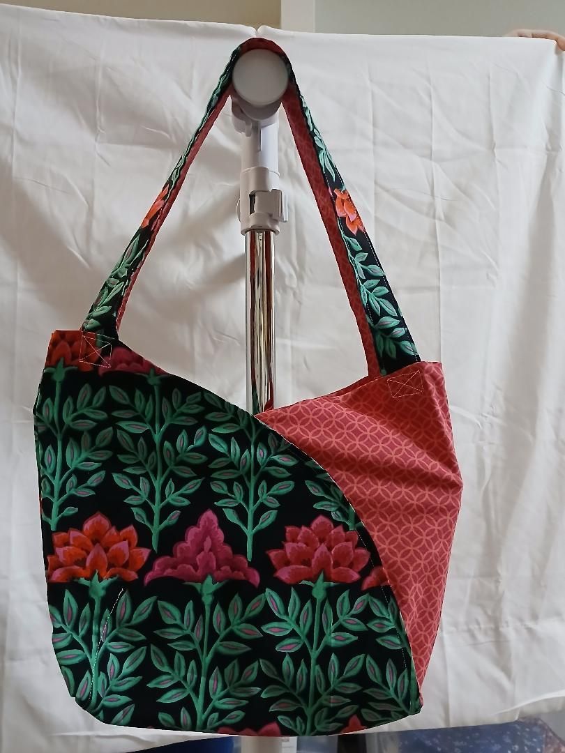 Colorful floral fabric tote bag hanging on a metal stand against a white backdrop