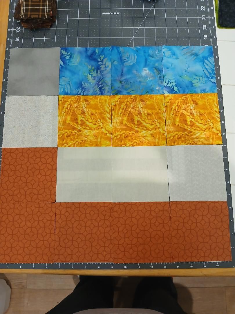 Colorful quilt blocks laid out on a cutting mat, with blue, yellow, white, and orange fabric sections.