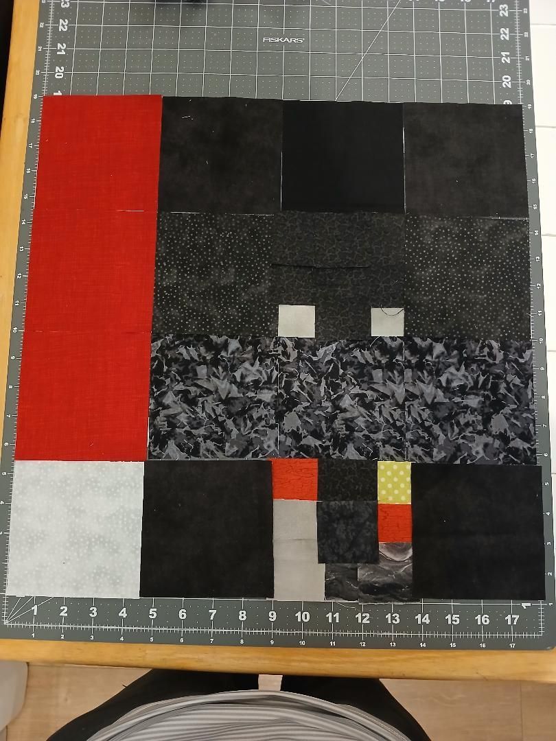 Abstract quilt with black, red, gray, and patterned blocks on a measuring mat