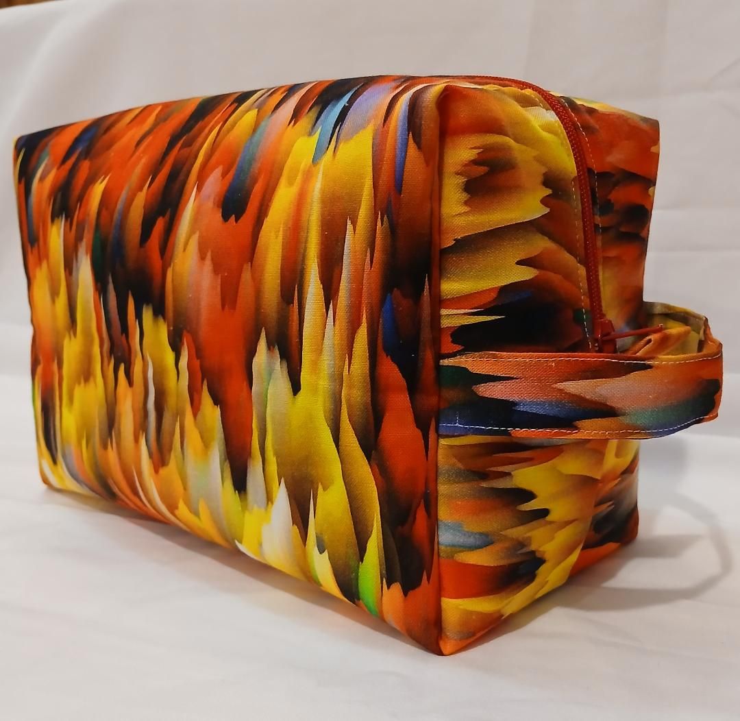Colorful patterned handbag with orange, yellow, and black feather-like design and a top handle