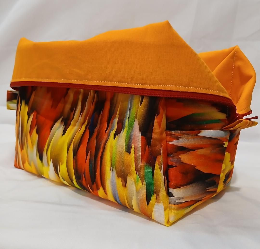 Orange fabric storage basket with colorful feather pattern and folded lid