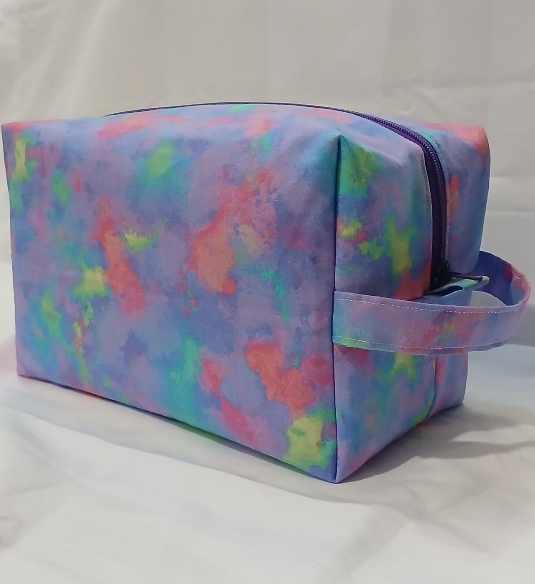 Colorful tie-dye cosmetic bag with a handle, resting on a white surface.