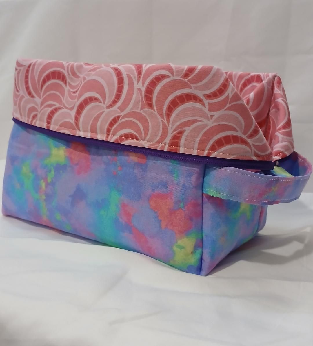Two colorful handmade fabric pouches with flap closures, one pink patterned and one blue-purple tie-dye.