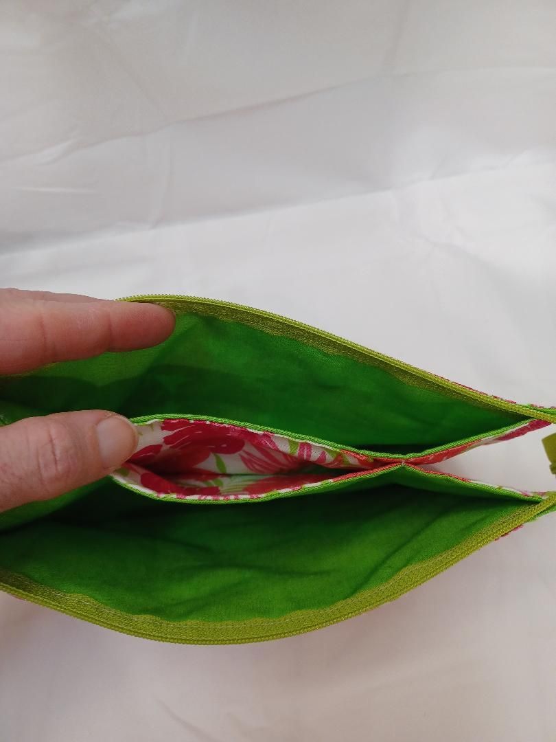 Hand holding open green-lined pouch with red floral fabric inside