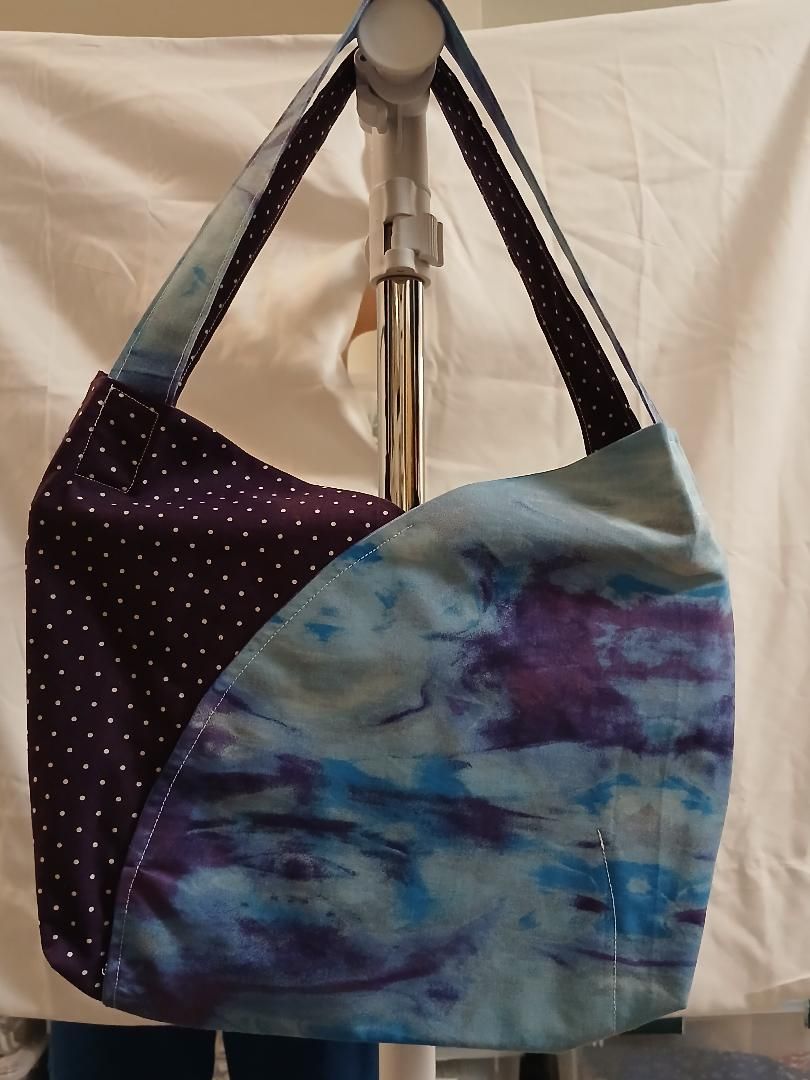 Colorful patchwork shoulder bag hanging on a stand, with blue-purple and black dotted fabric panels