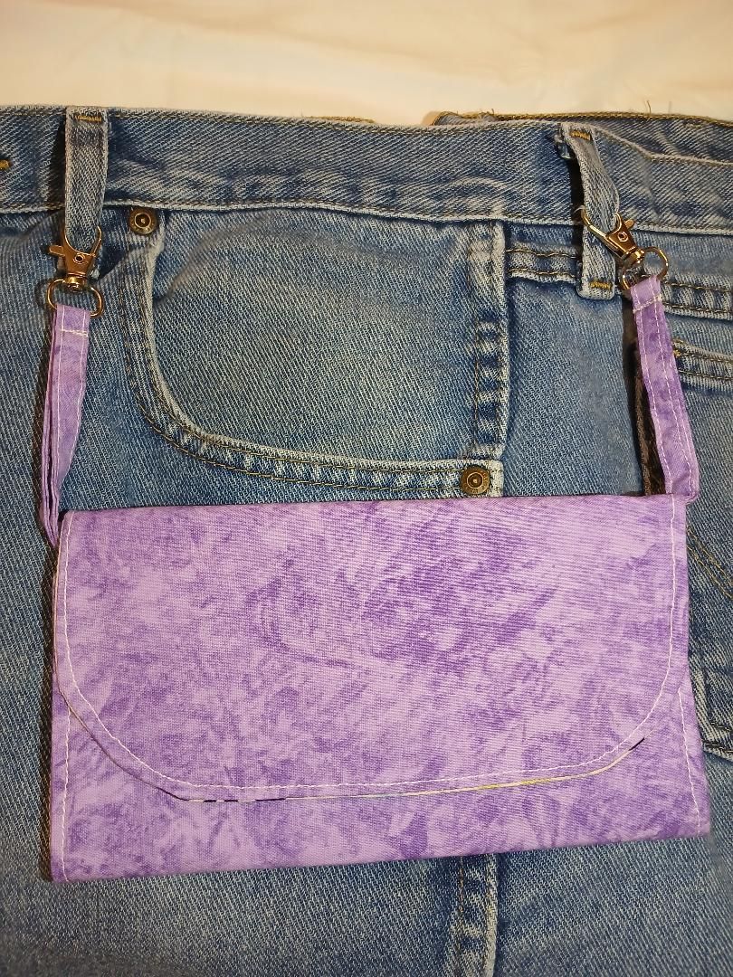 Purple fabric handbag made from denim and patchwork, hanging against a textured background