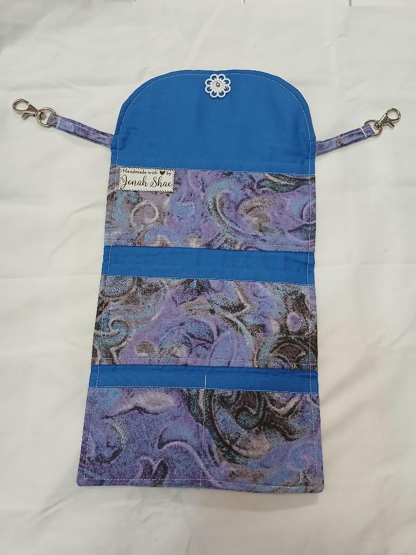 Blue and purple patterned hanging pouch with two side cords and a zipper closure